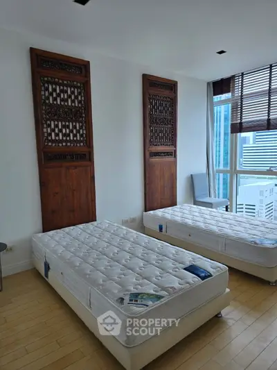 Spacious bedroom with twin beds and city view, featuring unique wooden headboards and large windows.