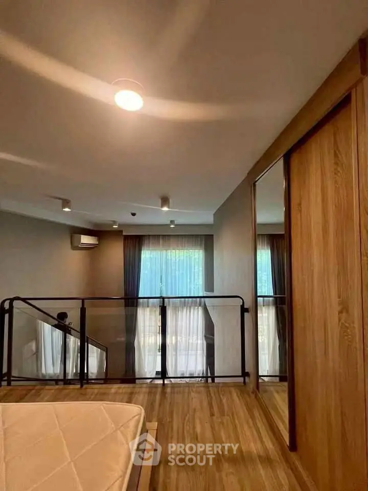 Modern loft-style bedroom with wooden flooring and large windows for natural light.