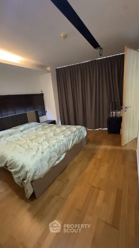 Spacious bedroom with wooden flooring and modern decor, featuring a large bed and stylish curtains.