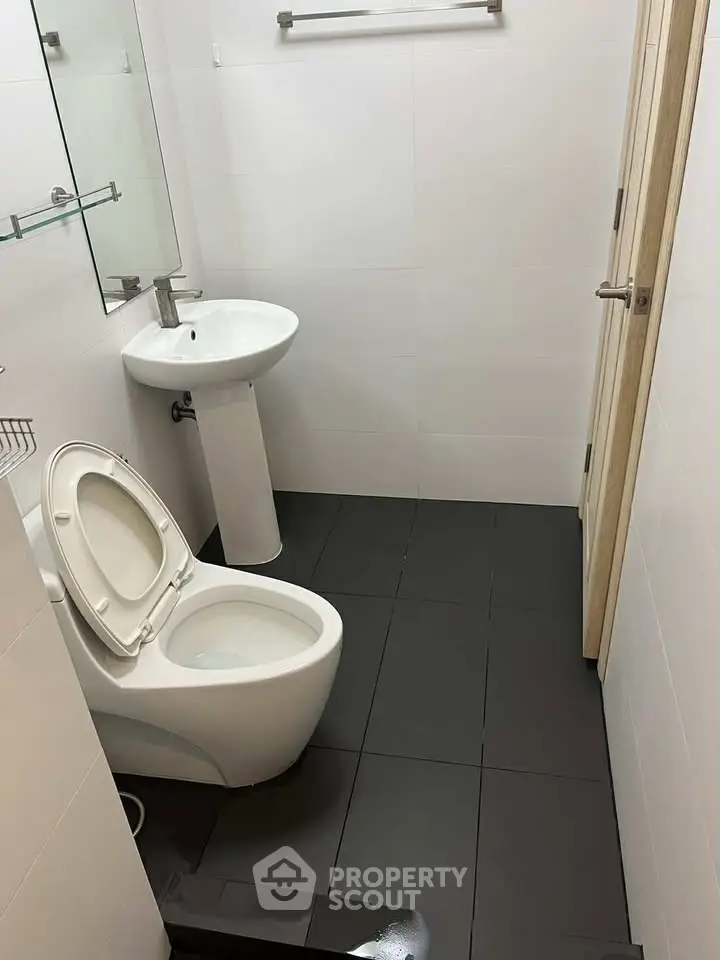 Modern bathroom with sleek fixtures and minimalist design, featuring a pedestal sink and contemporary toilet.