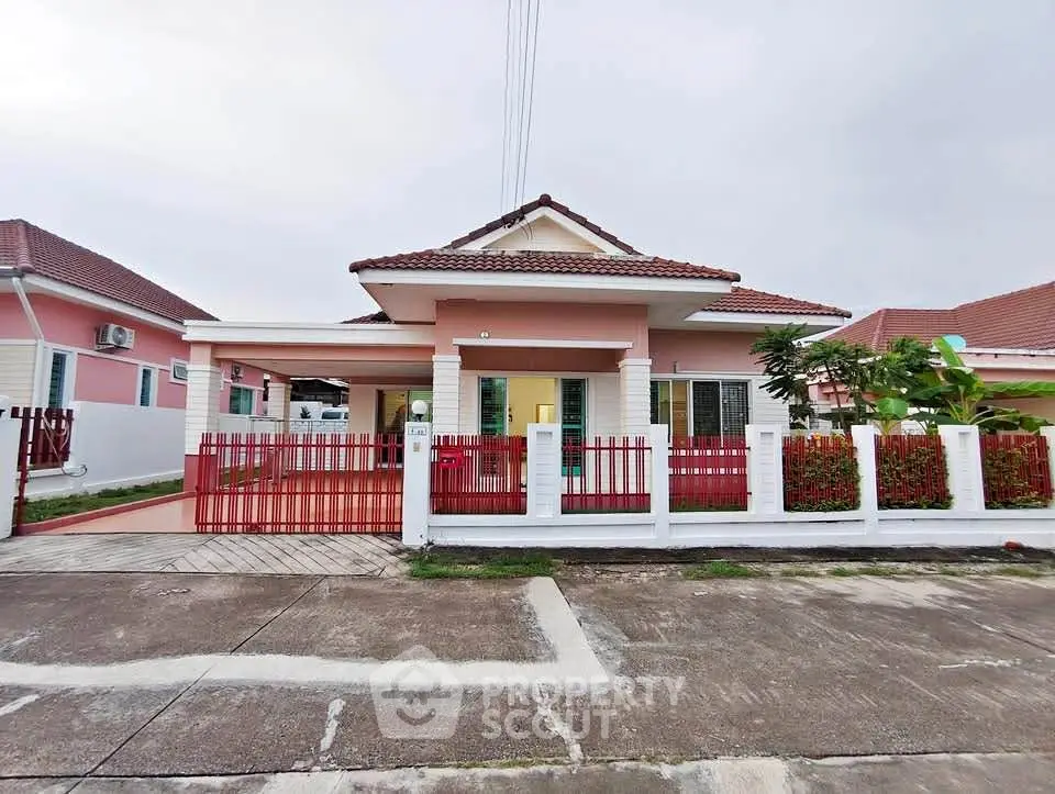 Charming single-story pink house with red fence and tiled roof in a serene neighborhood.