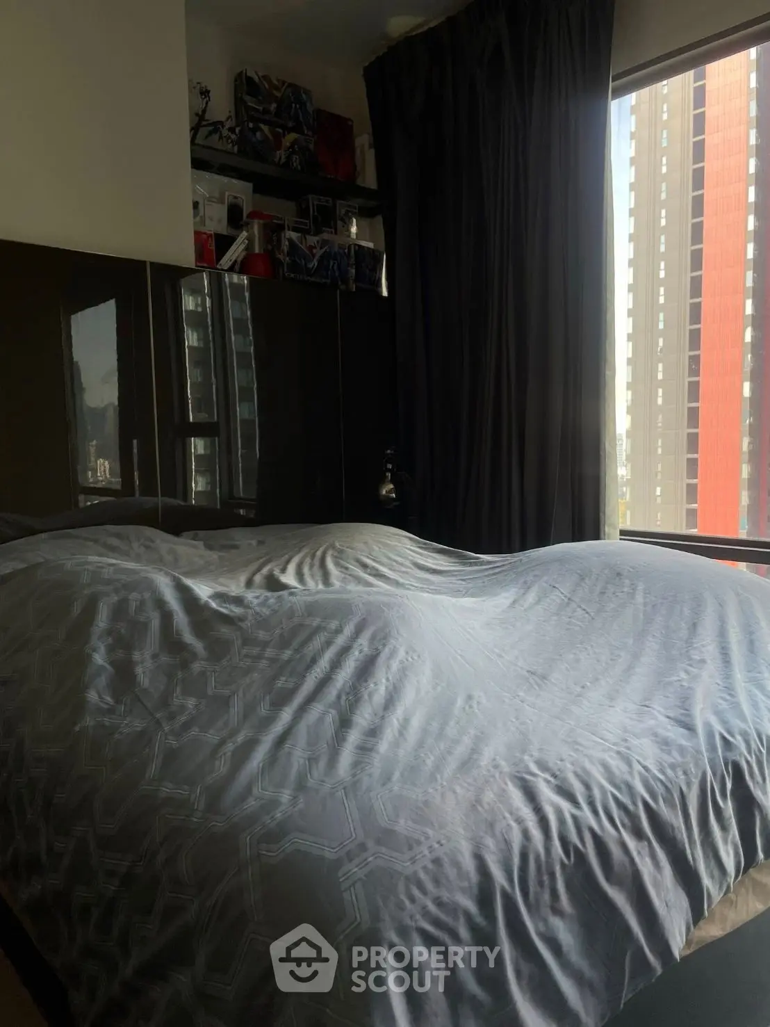 Modern bedroom with large window and city view, featuring sleek black cabinetry and cozy bedding.