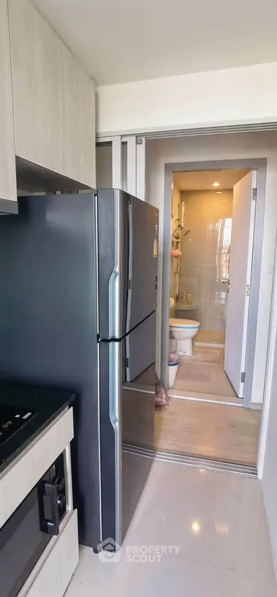 Modern kitchen with sleek appliances and view into compact bathroom