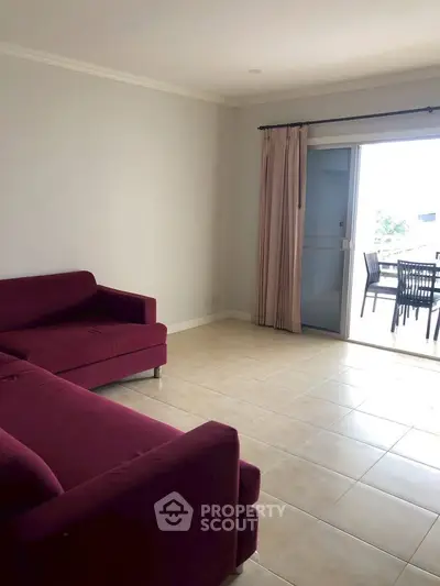 Spacious living room with red sofas and balcony access, ideal for relaxation and entertaining.