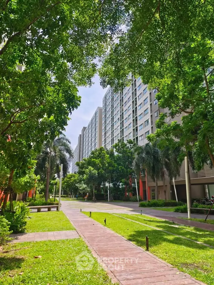 Lush green garden pathway leading to modern high-rise residential buildings.