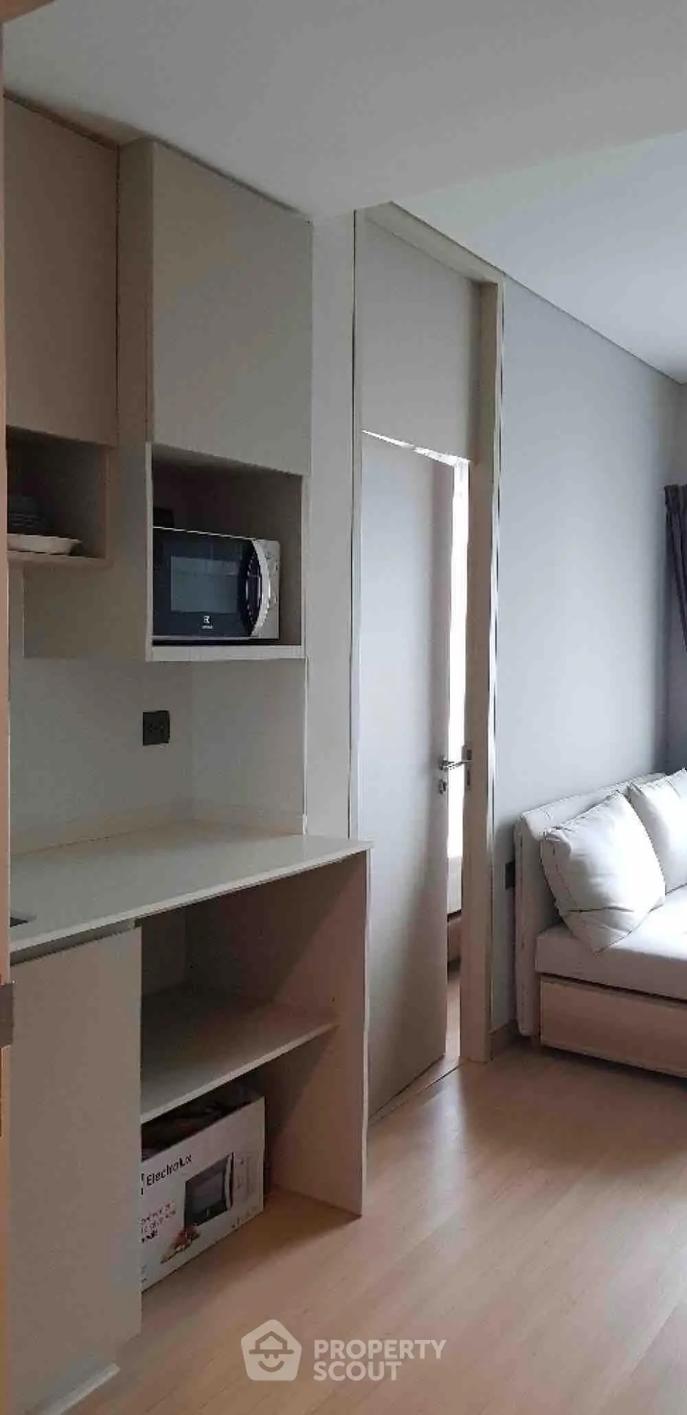 Modern apartment interior with sleek kitchen and cozy living area, featuring built-in microwave and stylish sofa.