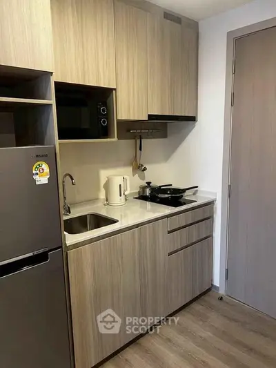Modern compact kitchen with wooden cabinets and sleek appliances in a cozy apartment.