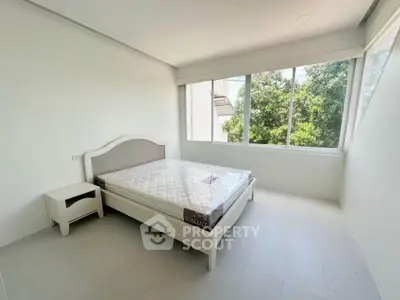 Bright minimalist bedroom with large windows and lush green view
