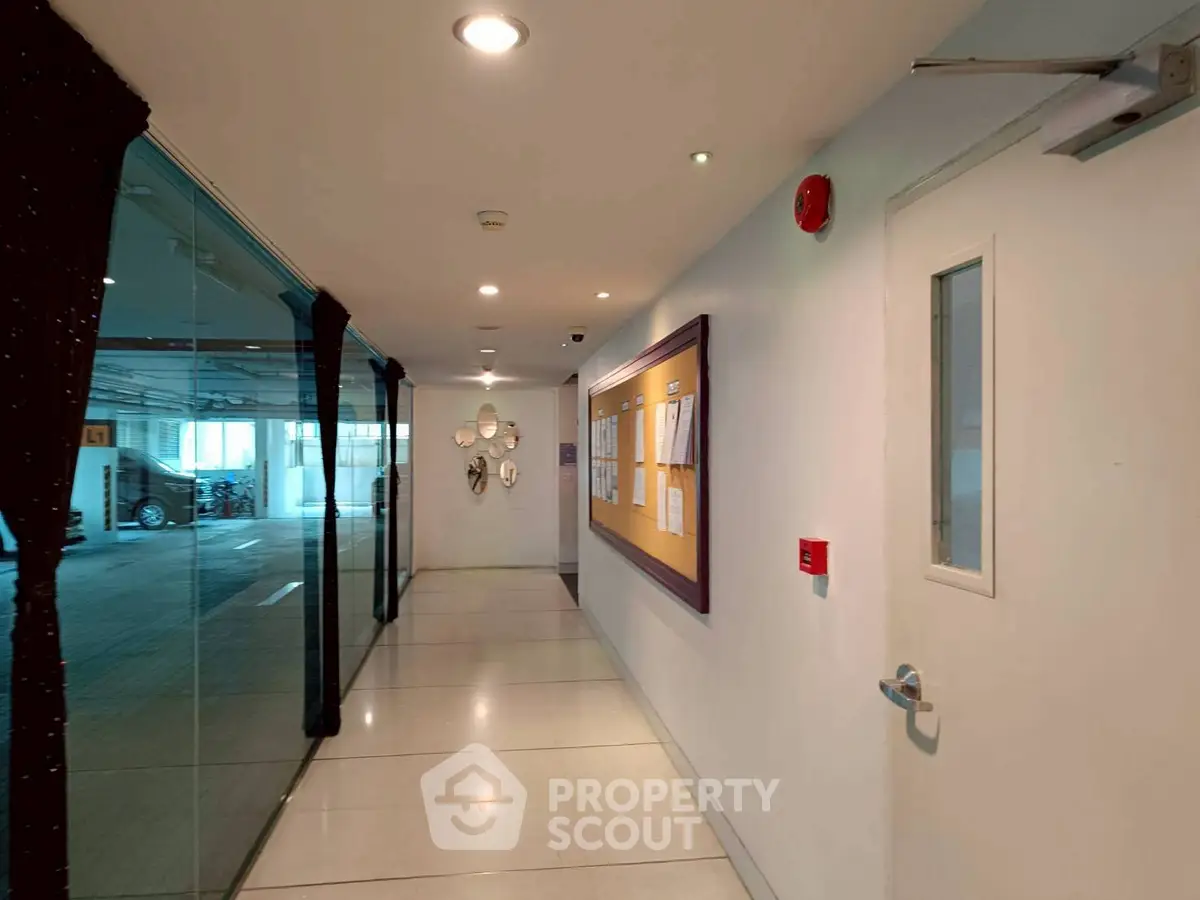 Modern building hallway with glass wall and bulletin board, leading to parking area.