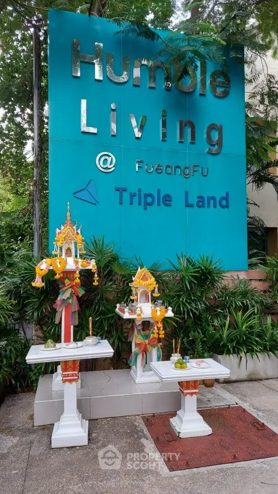 Modern apartment complex entrance with decorative spirit houses and lush greenery