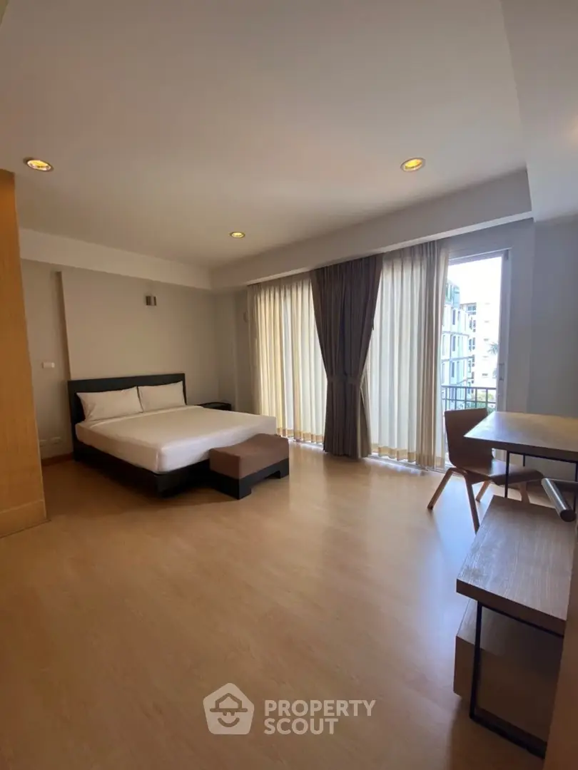 Spacious modern bedroom with large windows and wooden flooring in a stylish apartment.