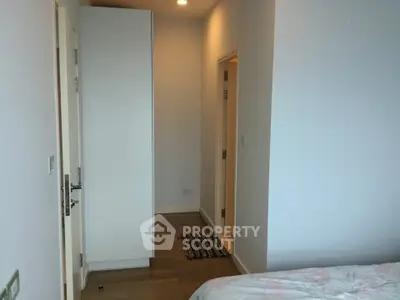 Cozy bedroom with wooden flooring and white walls, featuring a wardrobe and a glimpse of the hallway.