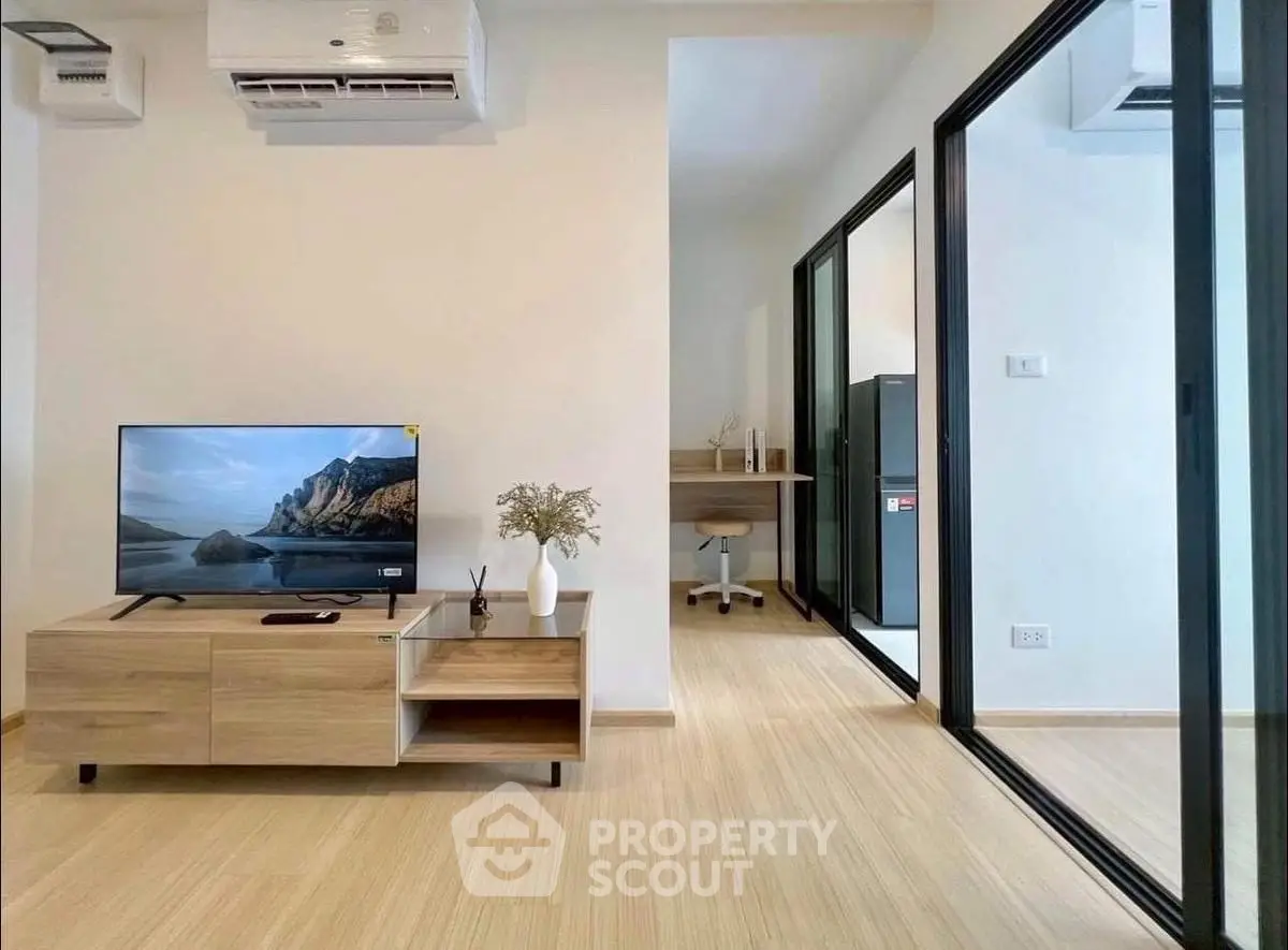 Modern living room with sleek TV stand and glass partition leading to study area.