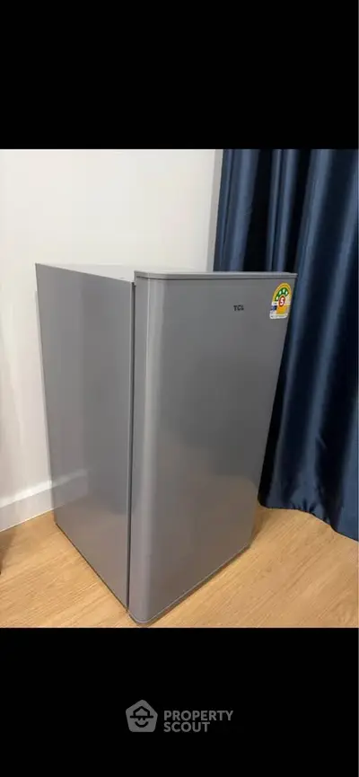 Modern compact refrigerator in sleek kitchen corner with wooden flooring and elegant curtains.