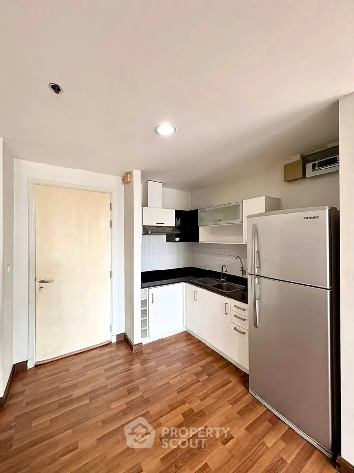 Modern kitchen with sleek cabinetry and stainless steel fridge in a cozy apartment.
