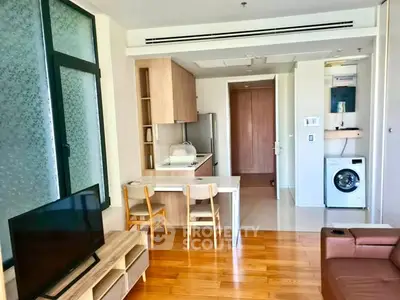 Modern living room with open kitchen and washing machine, featuring wooden flooring and stylish furniture.