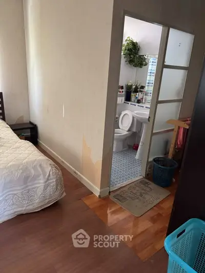 Cozy bedroom with adjacent bathroom, featuring wooden flooring and simple decor, ideal for comfortable living.