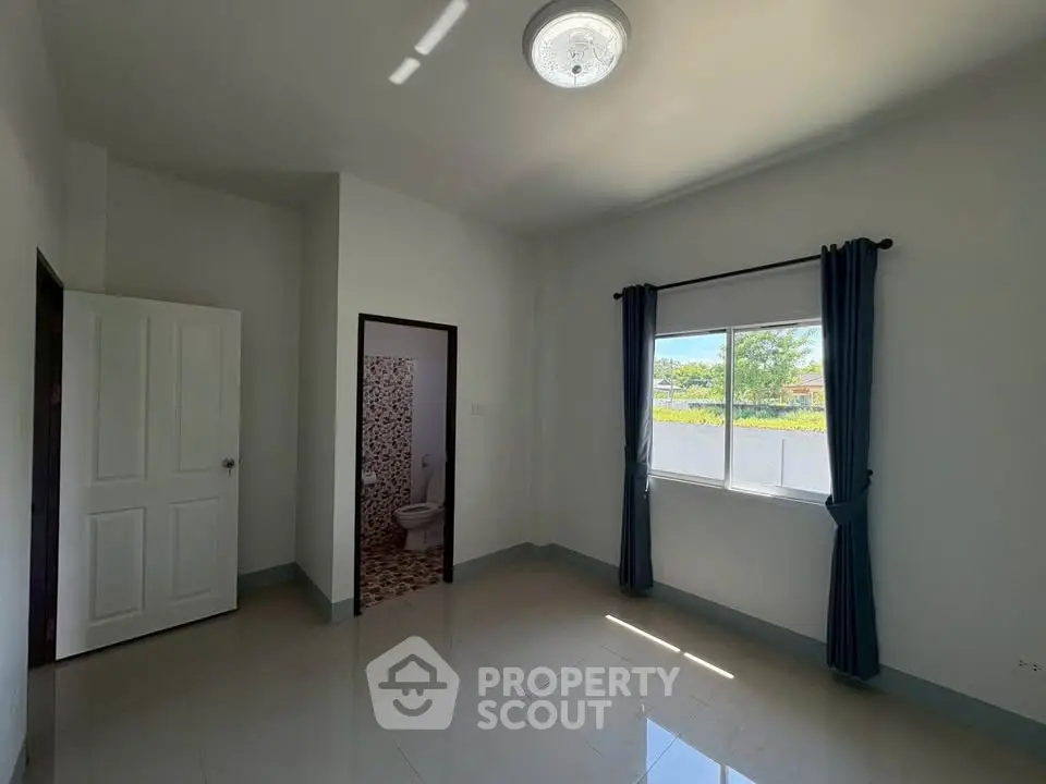 Spacious bedroom with natural light and modern design, featuring a window view and attached bathroom.