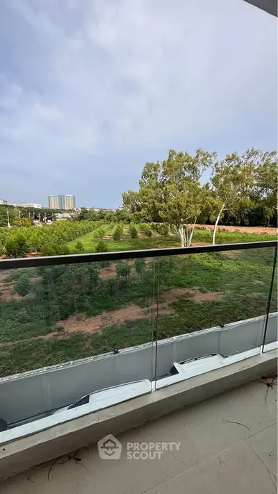 Spacious balcony with glass railing offering a serene view of lush greenery and distant buildings.