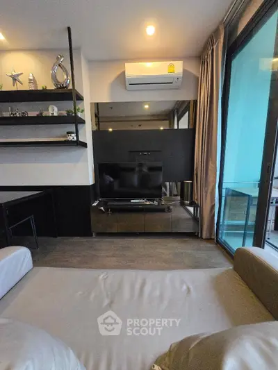 Modern living room with sleek design, featuring a large TV, air conditioning, and balcony access.