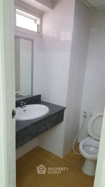 Compact bathroom with modern sink and toilet, featuring clean white tiles and a small window for natural light.
