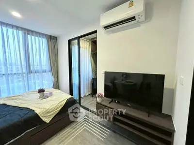 Modern bedroom with large windows and sleek furniture, featuring a wall-mounted TV and air conditioning.