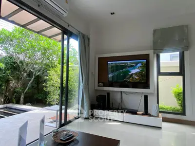 Modern living room with large windows and garden view, featuring sleek TV setup and stylish decor.