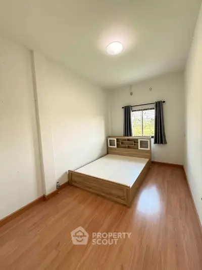 Spacious bedroom with wooden flooring and modern bed frame, featuring natural light from window.