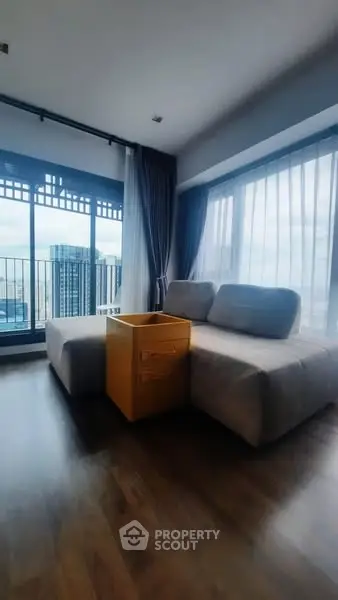Modern living room with large windows and city view, featuring a cozy sofa and stylish decor.