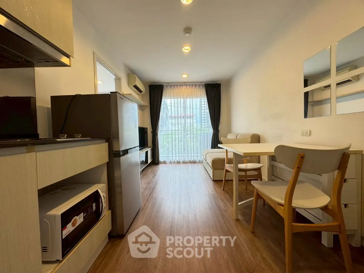 Modern living room with wooden flooring, cozy seating, and natural light from large window.