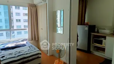 Cozy bedroom with large window, modern furnishings, and compact kitchen area in urban apartment.