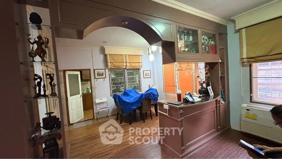 Charming living room with wooden flooring and elegant archway, featuring cozy dining area and natural light.