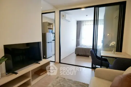Modern apartment interior with open living room and bedroom, featuring sleek furniture and natural light.
