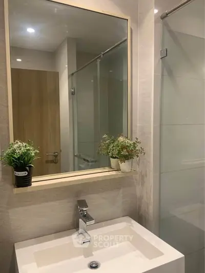 Modern bathroom with sleek sink and large mirror, featuring elegant decor and glass shower enclosure.