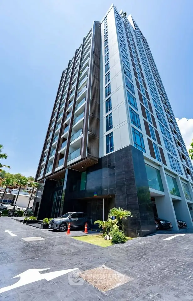 Modern high-rise building with sleek design and spacious parking area under clear blue sky.