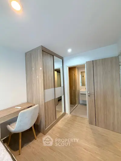 Modern bedroom with wooden flooring, built-in wardrobe, and study desk in a stylish apartment.