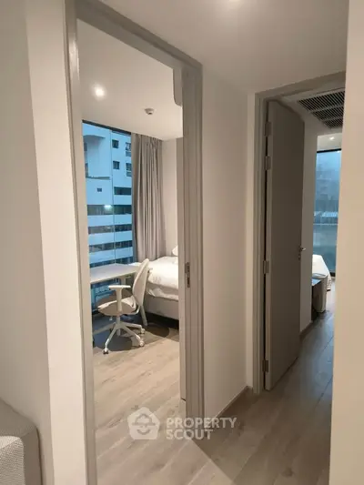 Modern apartment hallway leading to a cozy bedroom with study desk and chair, showcasing urban living.