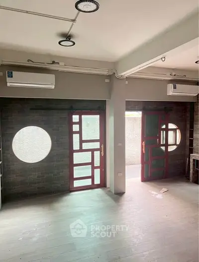 Spacious modern living room with unique circular windows and sliding doors, featuring dual air conditioning units.