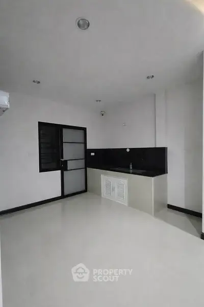 Minimalist kitchen with sleek black countertops and white cabinetry in modern apartment.
