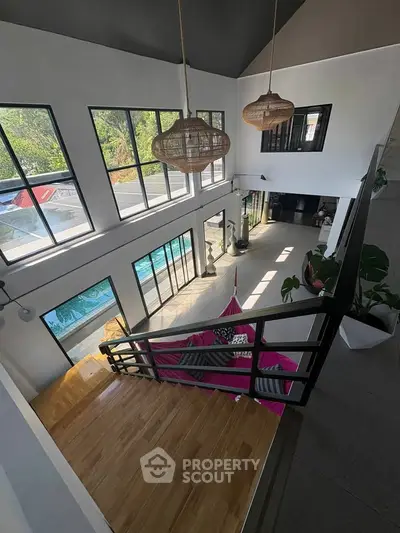 Stunning modern living room with high ceilings and large windows overlooking a pool, featuring elegant decor.