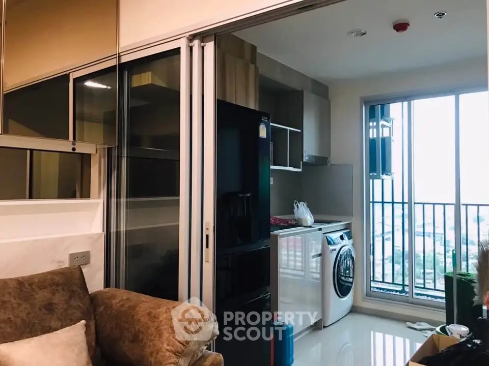 Modern apartment with open kitchen and laundry area, featuring a washing machine and balcony view.
