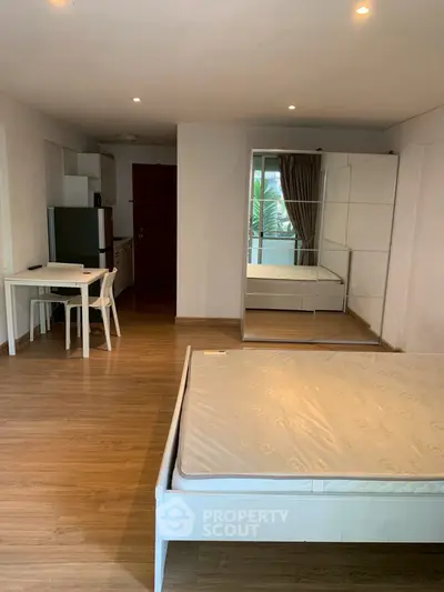 Spacious studio apartment with wooden flooring and modern furnishings, featuring a mirrored wardrobe and cozy dining area.