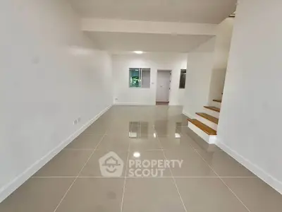 Spacious modern living room with glossy tiled floors and staircase, perfect for family gatherings.