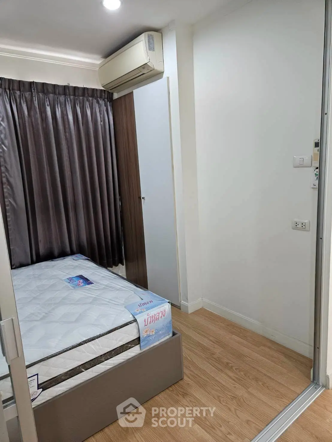 Cozy bedroom with wooden flooring and air conditioning, featuring a comfortable bed and elegant curtains.