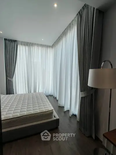 Spacious bedroom with floor-to-ceiling windows and elegant curtains, featuring a modern bed and stylish floor lamp.