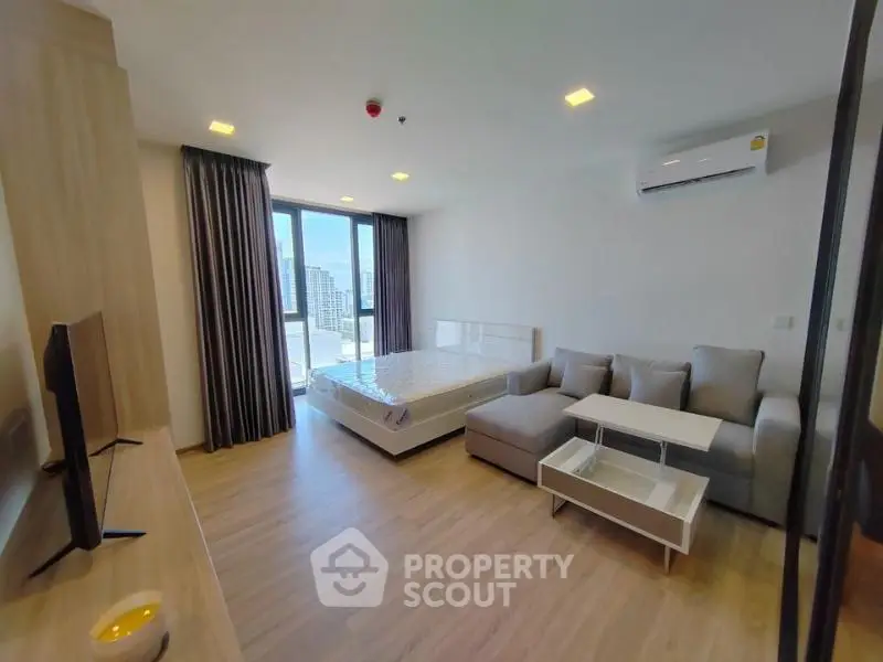 Modern studio apartment with large windows and city view, featuring a cozy living area and stylish furnishings.
