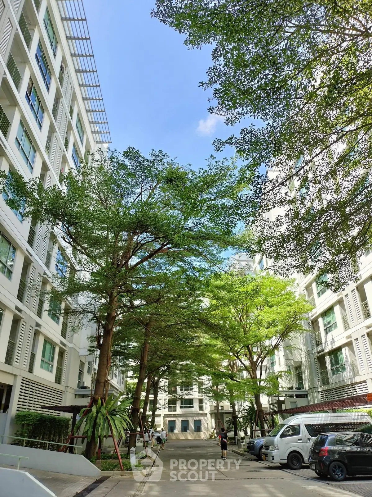 Modern residential building with lush greenery and parked cars under a clear blue sky.
