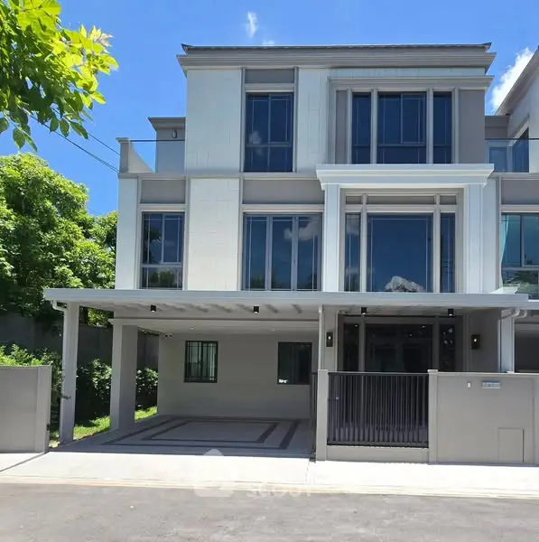 Modern three-story house with large windows and a spacious driveway under clear blue skies.