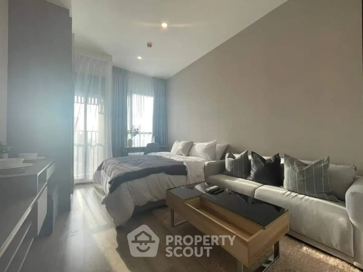 Modern studio apartment with cozy living area and bed, featuring natural light and stylish decor.