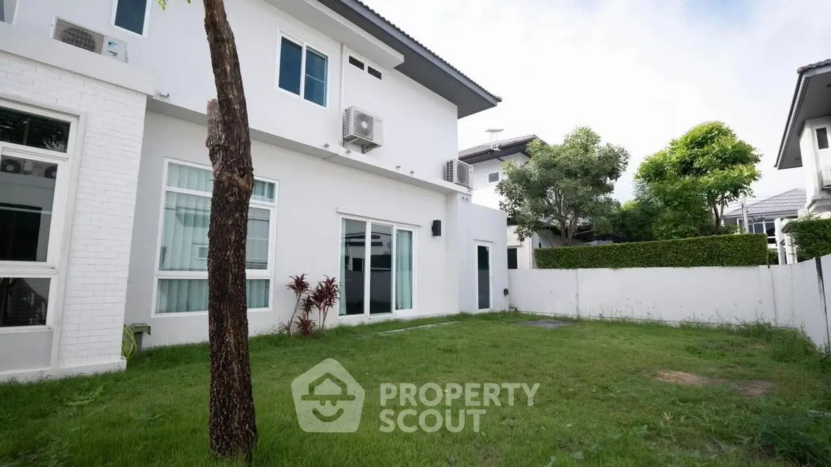 Spacious backyard of modern two-story home with lush green lawn and white exterior.